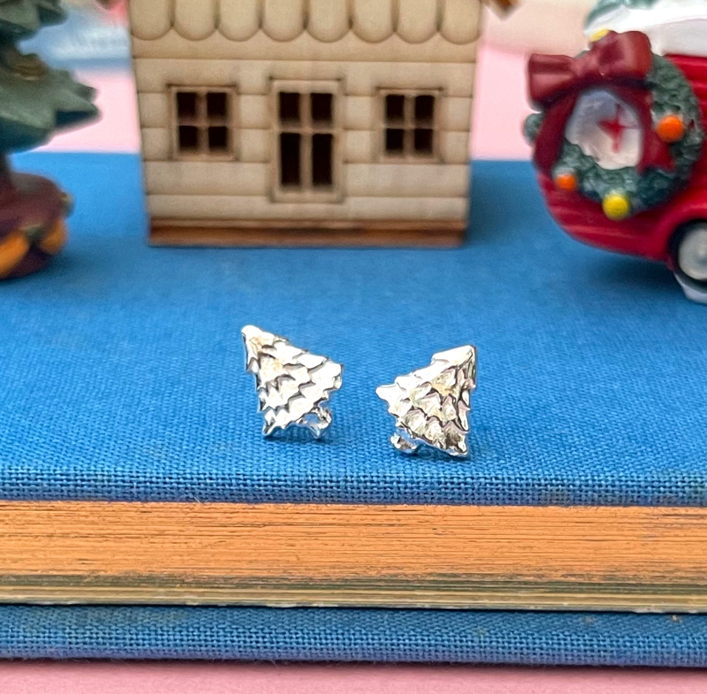 Silver triangle-shaped earrings on a blue surface with a toy house and car in the background.